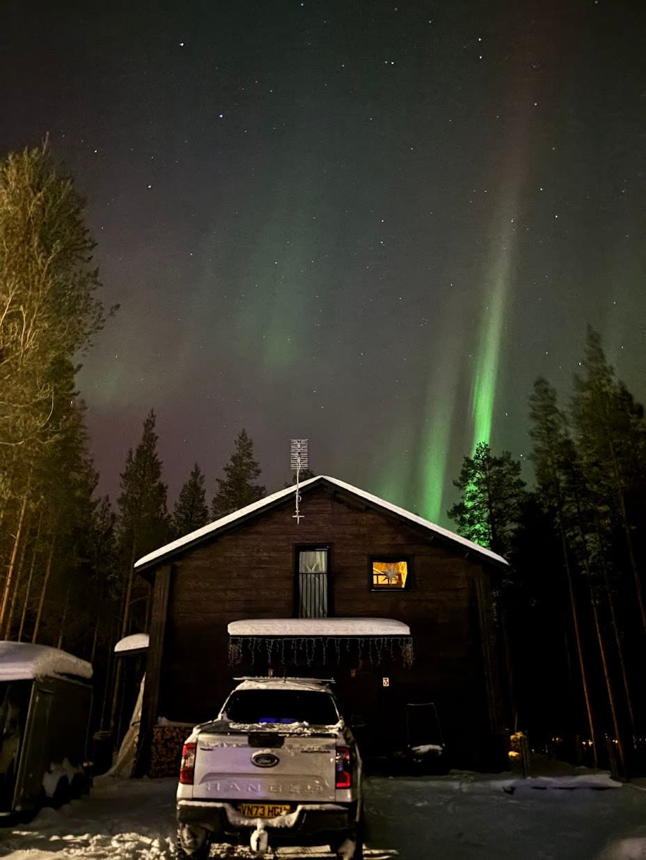 The aurora borealis in green ribbons above the Snow & Pine cabin on a clear Arctic night in Levi